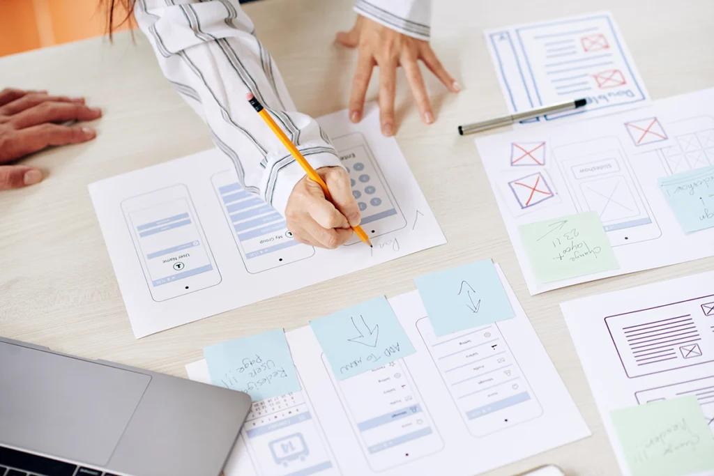 Zespół projektowy pracujący nad makietami (wireframe) interfejsu aplikacji mobilnej na papierze