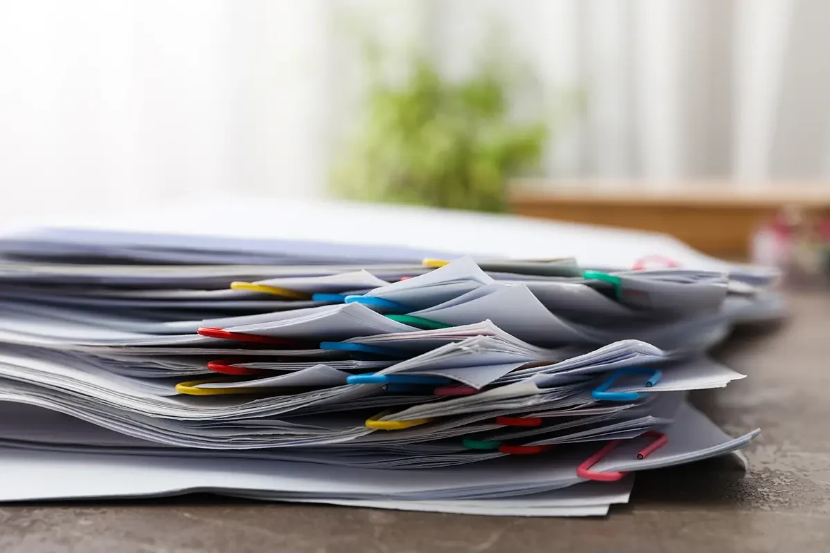 Duży stos nieuporządkowanych papierów spiętych kolorowymi spinaczami – ilustracja problemu ręcznego przetwarzania faktur przed wdrożeniem OCR i automatyzacji