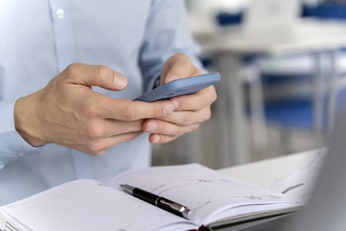 Zbliżenie na dłonie trzymające smartfon nad otwartym kalendarzem – symbol cyfrowego przetwarzania dokumentów i automatyzacji faktur w firmie